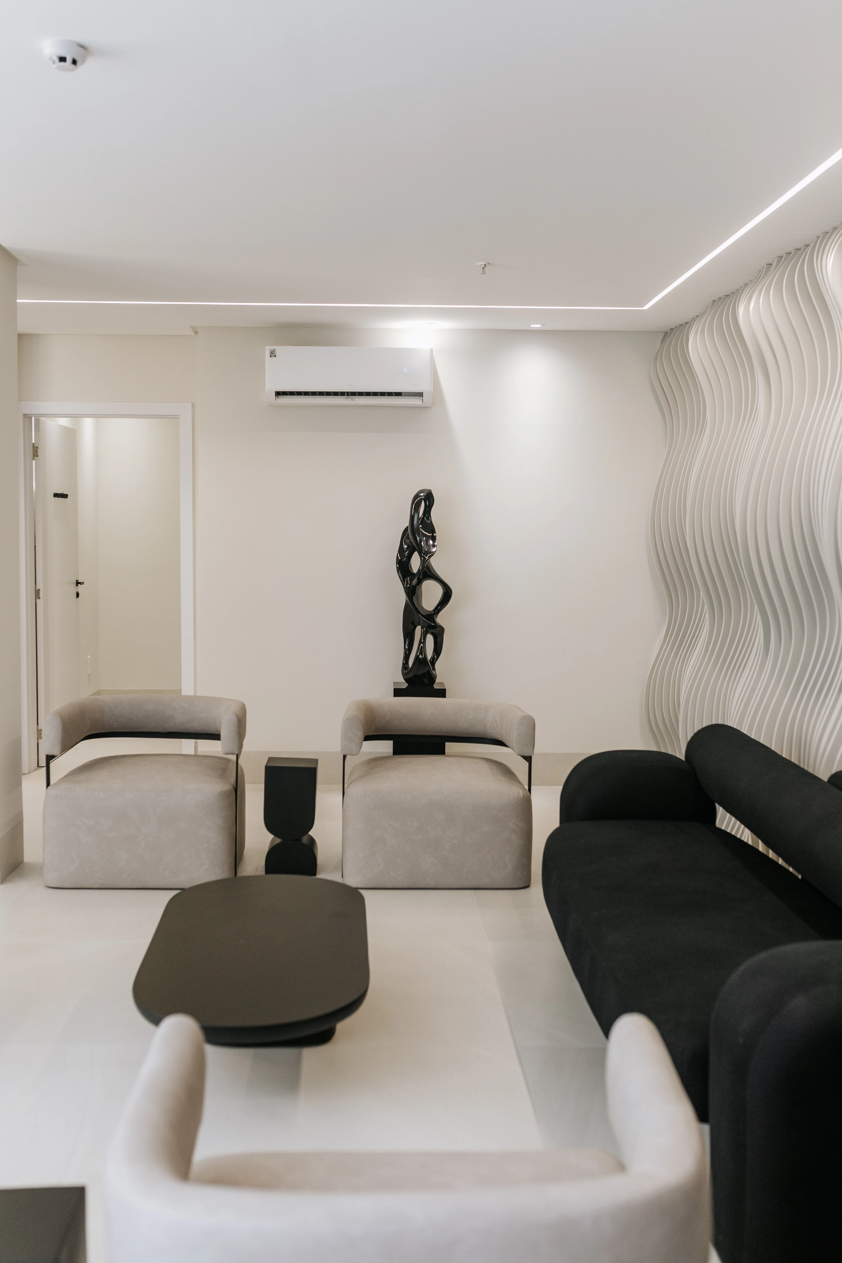 Recepção com poltronas claras, sofá escuro e parede com formas orgânicas